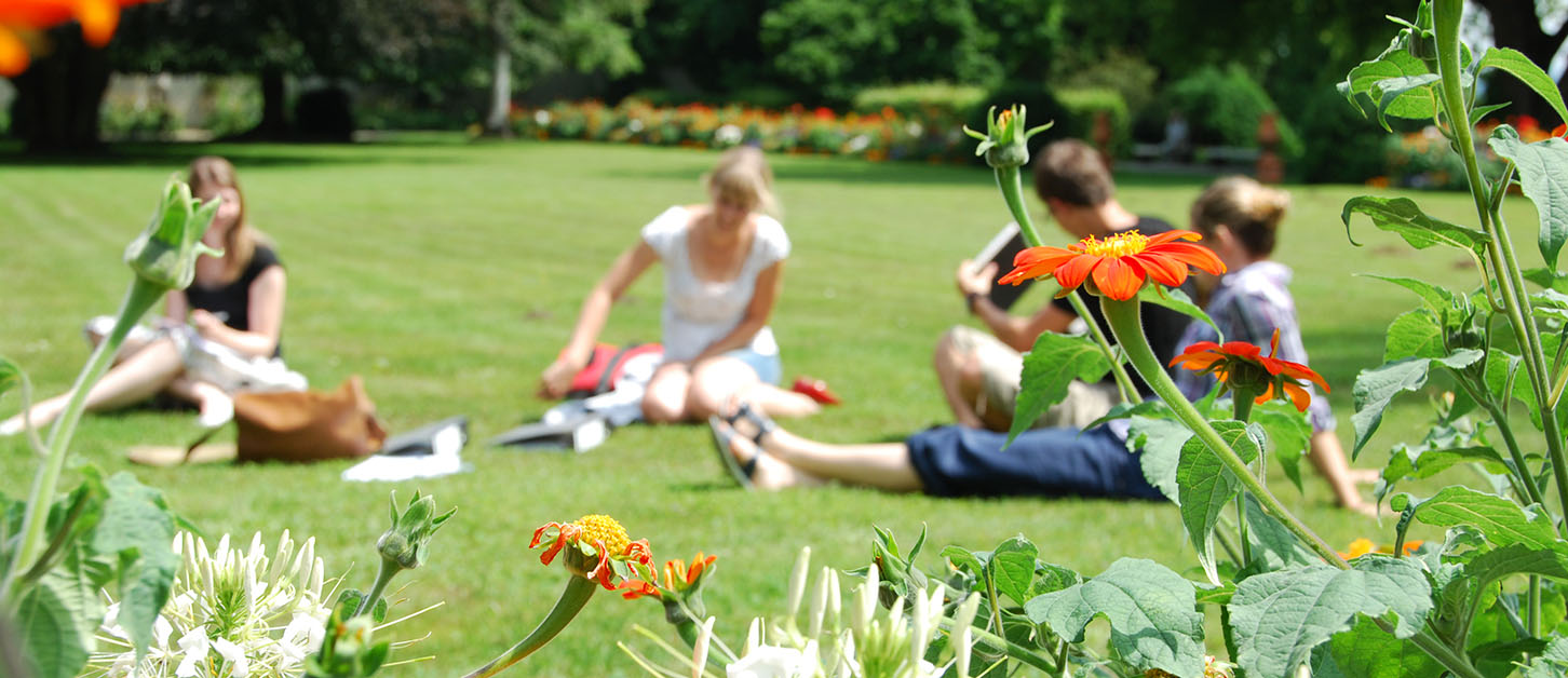 Garten der Hochschule Weihenstephan-Triesdorf, vier Studierende auf dem Rasen sitzend, Blumen ragen im Vordergrund ins Bild