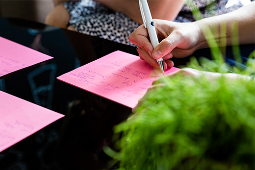 Hand notiert etwas auf pinkfarbenen Papier